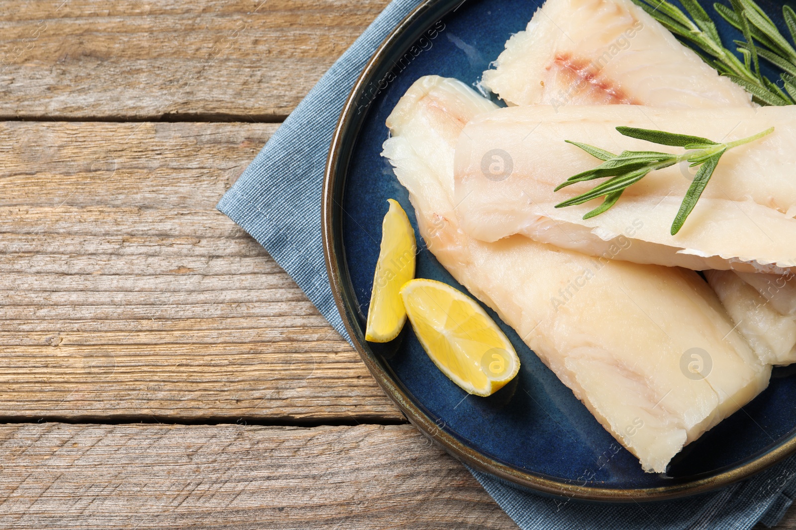 Photo of Pieces of raw cod fish, rosemary and lemon on wooden table, top view. Space for text