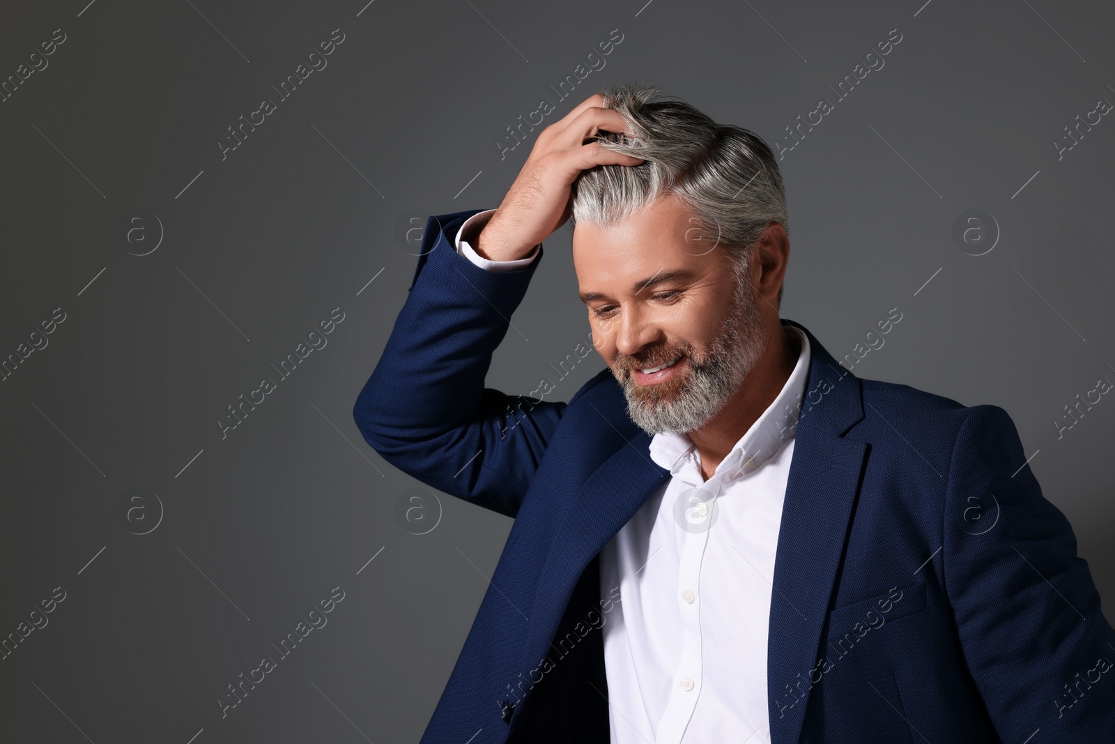 Photo of Portrait of smiling man with beautiful hairstyle on dark grey background