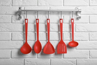 Rack with kitchen utensils hanging on white brick wall