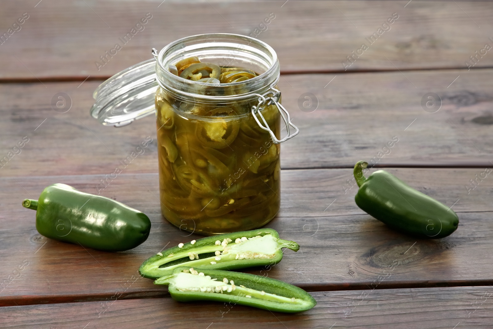 Photo of Fresh and pickled green jalapeno peppers on wooden table