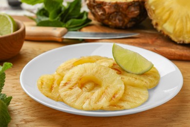 Tasty grilled pineapple slices and piece of lime on wooden table, closeup