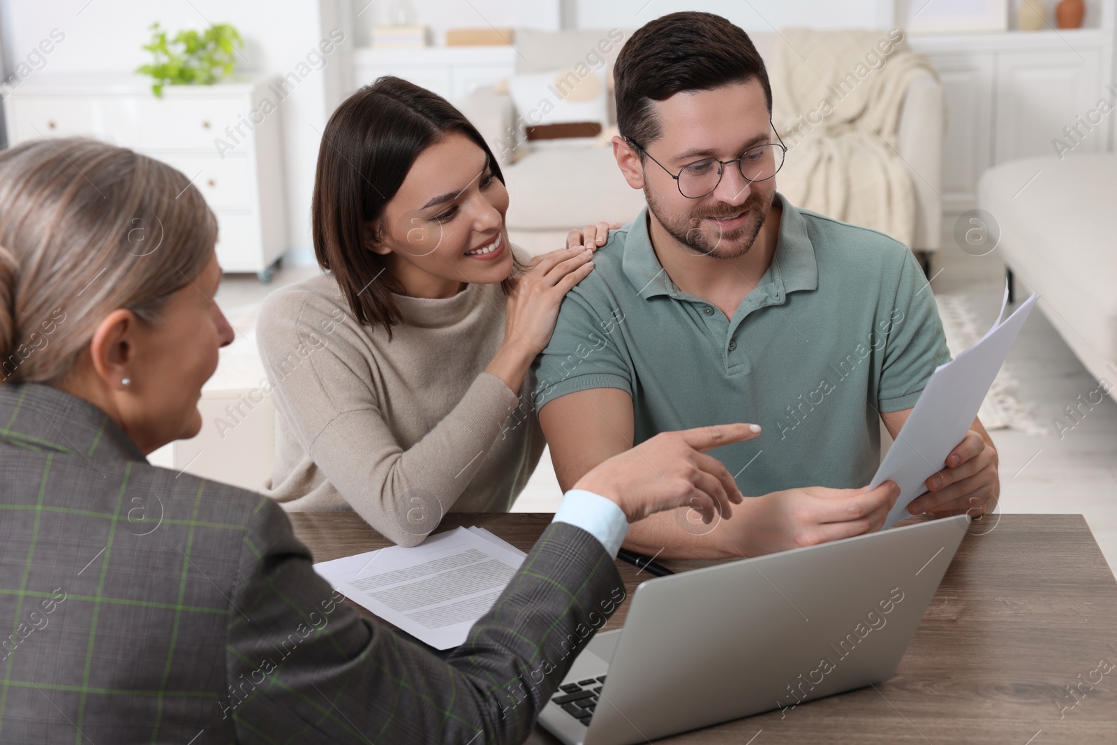 Photo of Young couple consulting insurance agent about pension plan at wooden table indoors