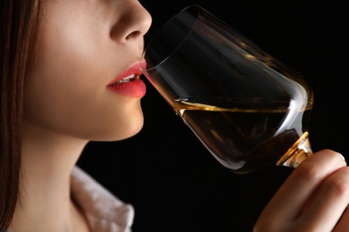 Photo of Young woman with glass of luxury white wine on black background, closeup view