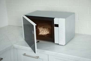 Photo of Open microwave oven with fresh popcorn on countertop in kitchen