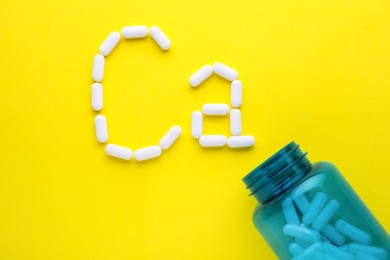 Photo of Open bottle and calcium symbol made of white pills on yellow background, flat lay