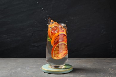Photo of Delicious refreshing drink with sicilian orange splashing out of glass on grey table against black background