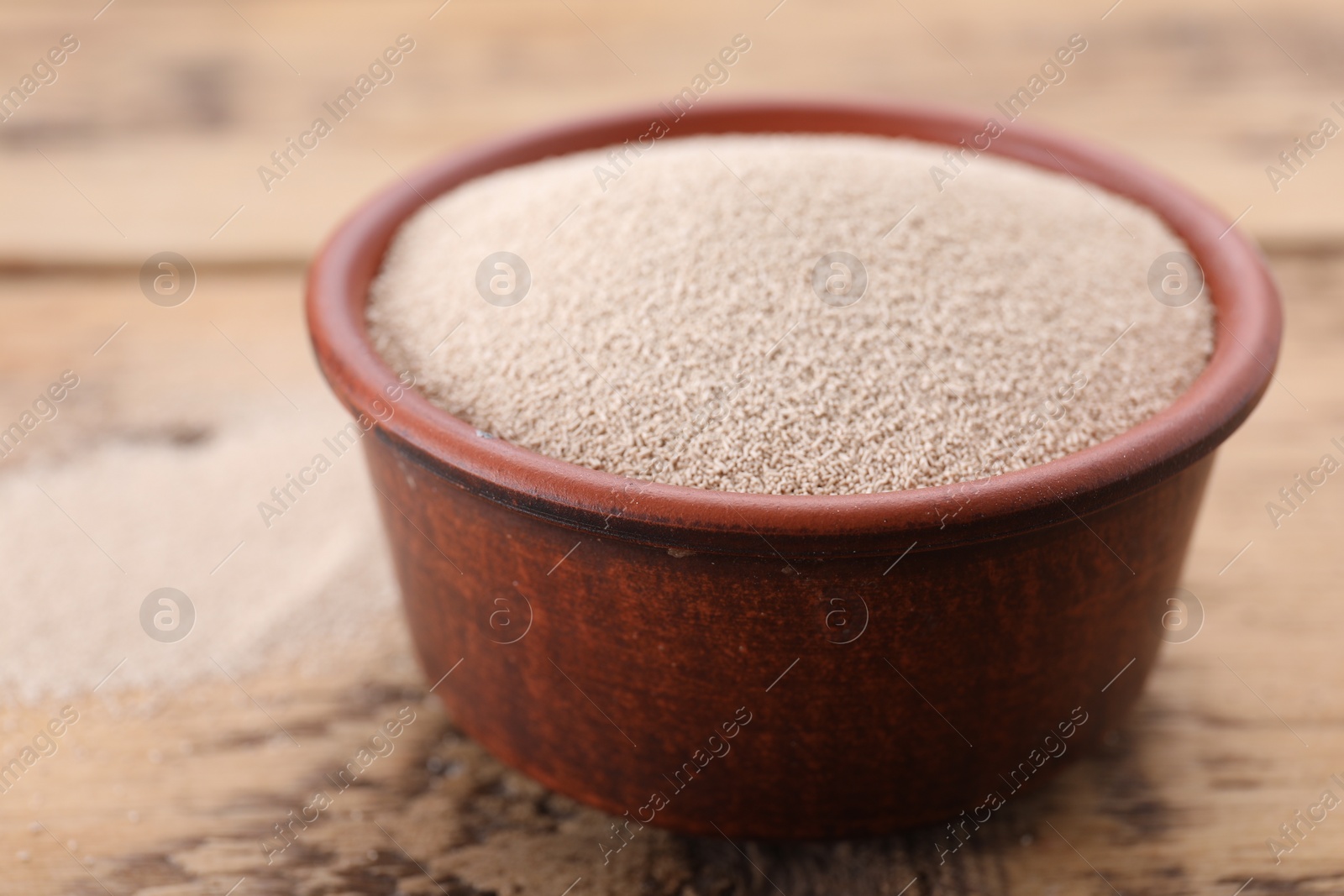 Photo of Bowl of active dry yeast on wooden table, closeup