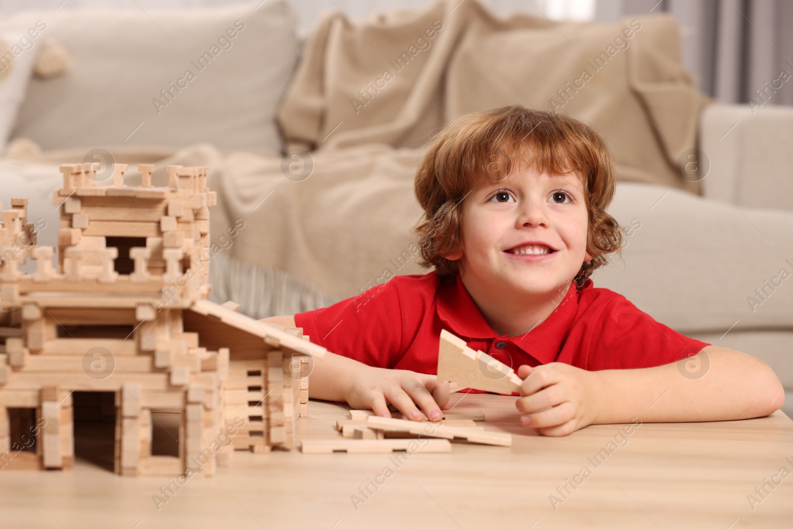 Photo of Cute little boy playing with wooden castle at table in room. Child's toy