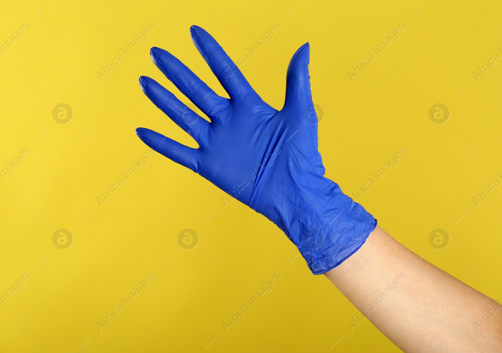 Photo of Woman in blue latex gloves on yellow background, closeup of hand