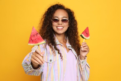 Photo of Beautiful young African American woman with pieces of watermelon against yellow background, focus on hand