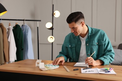 Photo of Man drawing in sketchbook with pencil at wooden table indoors