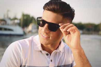 Handsome man wearing stylish sunglasses near river