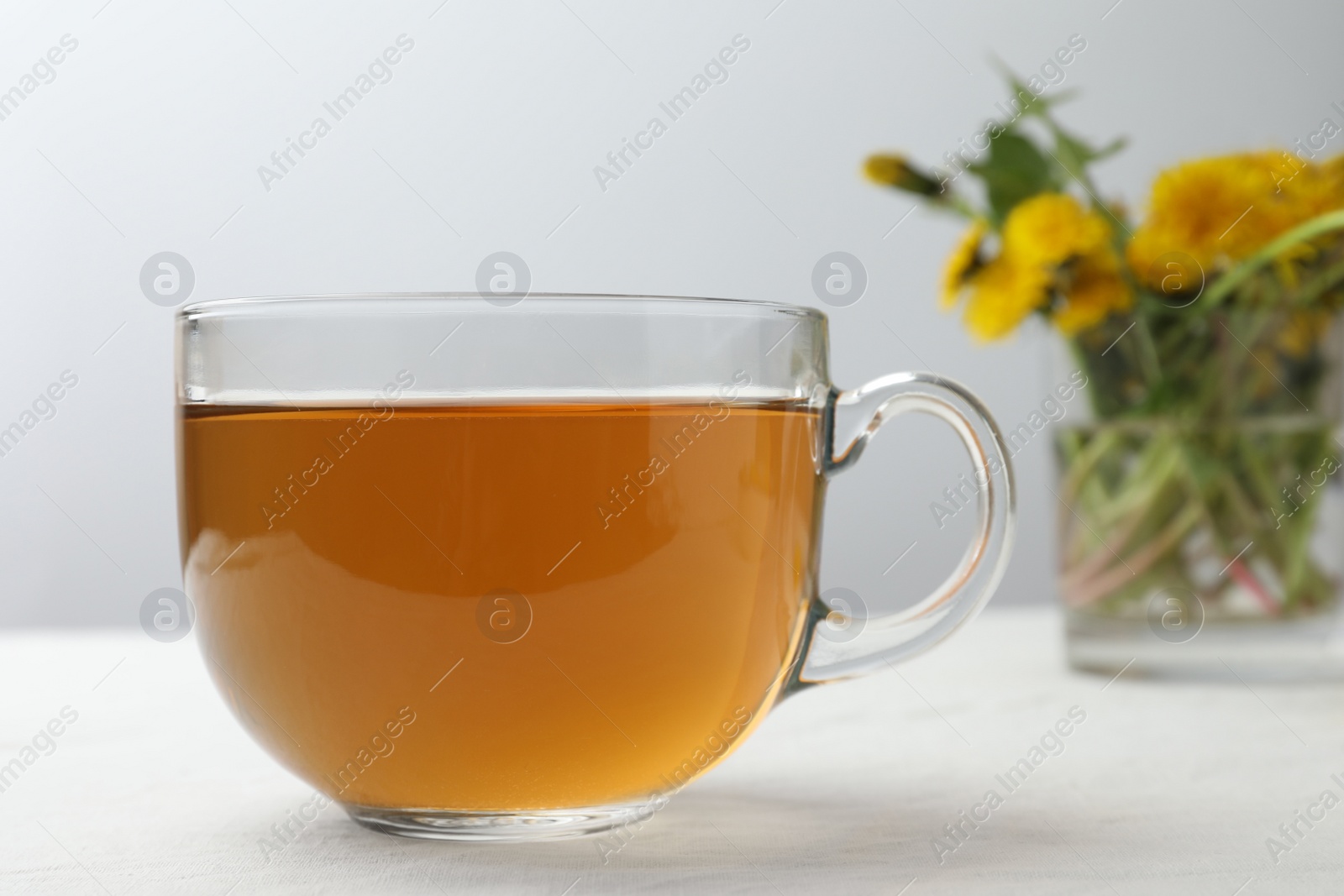 Photo of Delicious fresh tea and beautiful dandelion flowers on white table