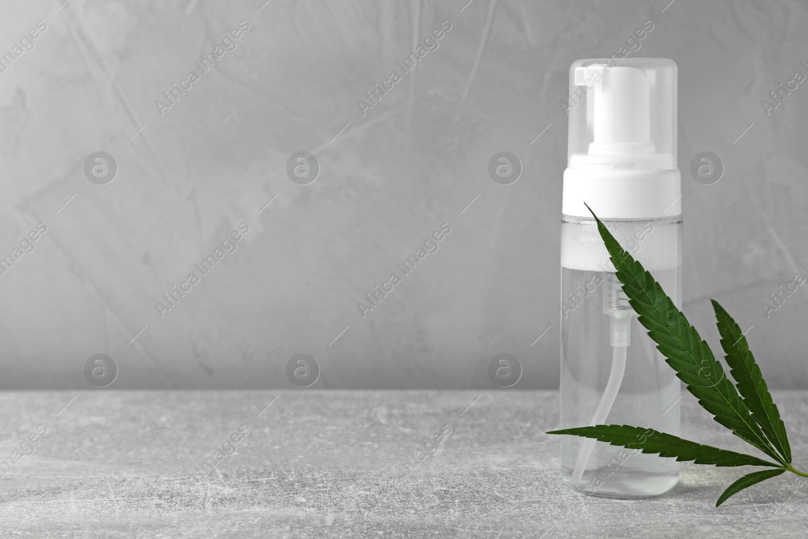 Photo of Hemp cosmetic product and leaf on grey table. Space for text