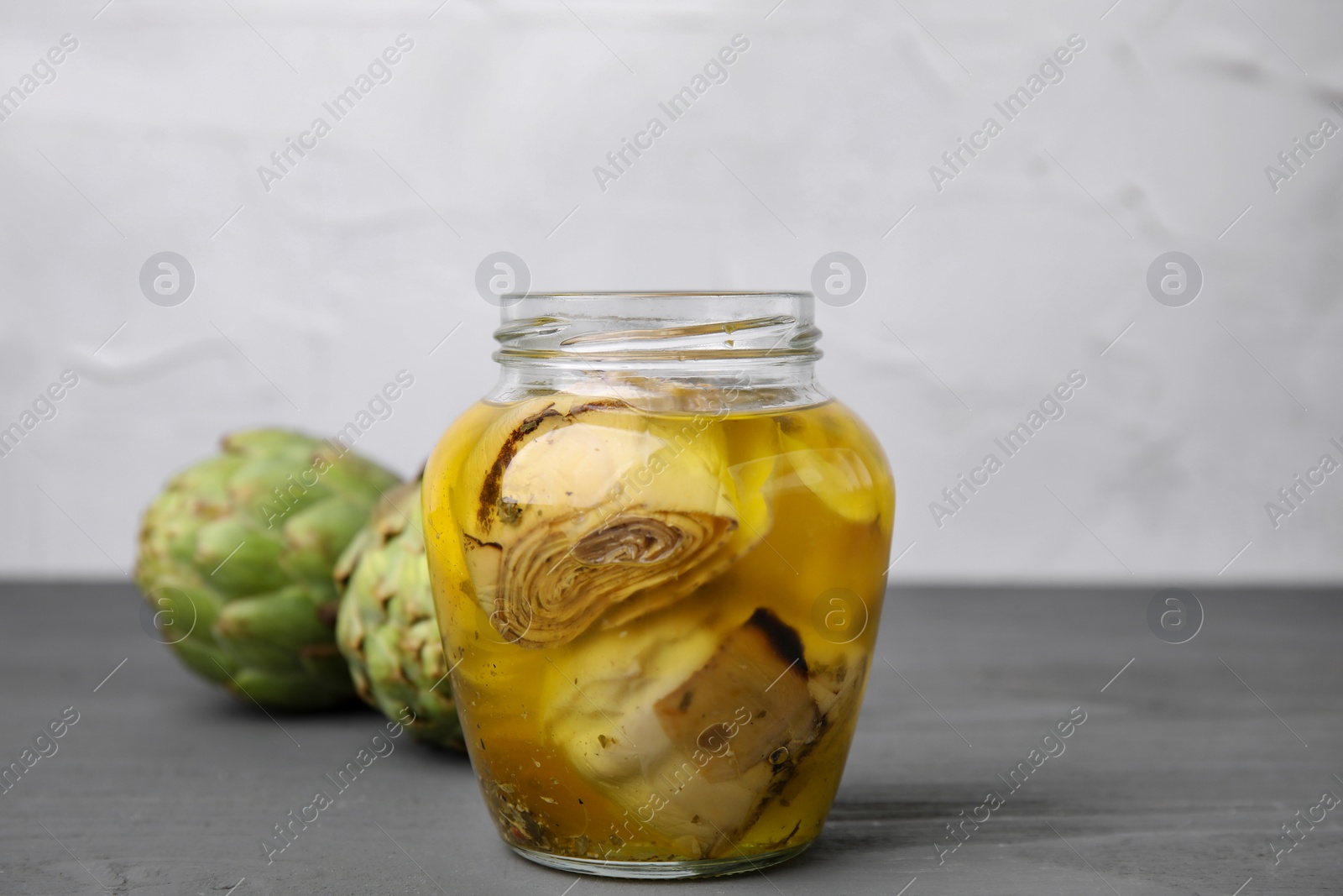 Photo of Pickled and fresh artichokes on grey wooden table