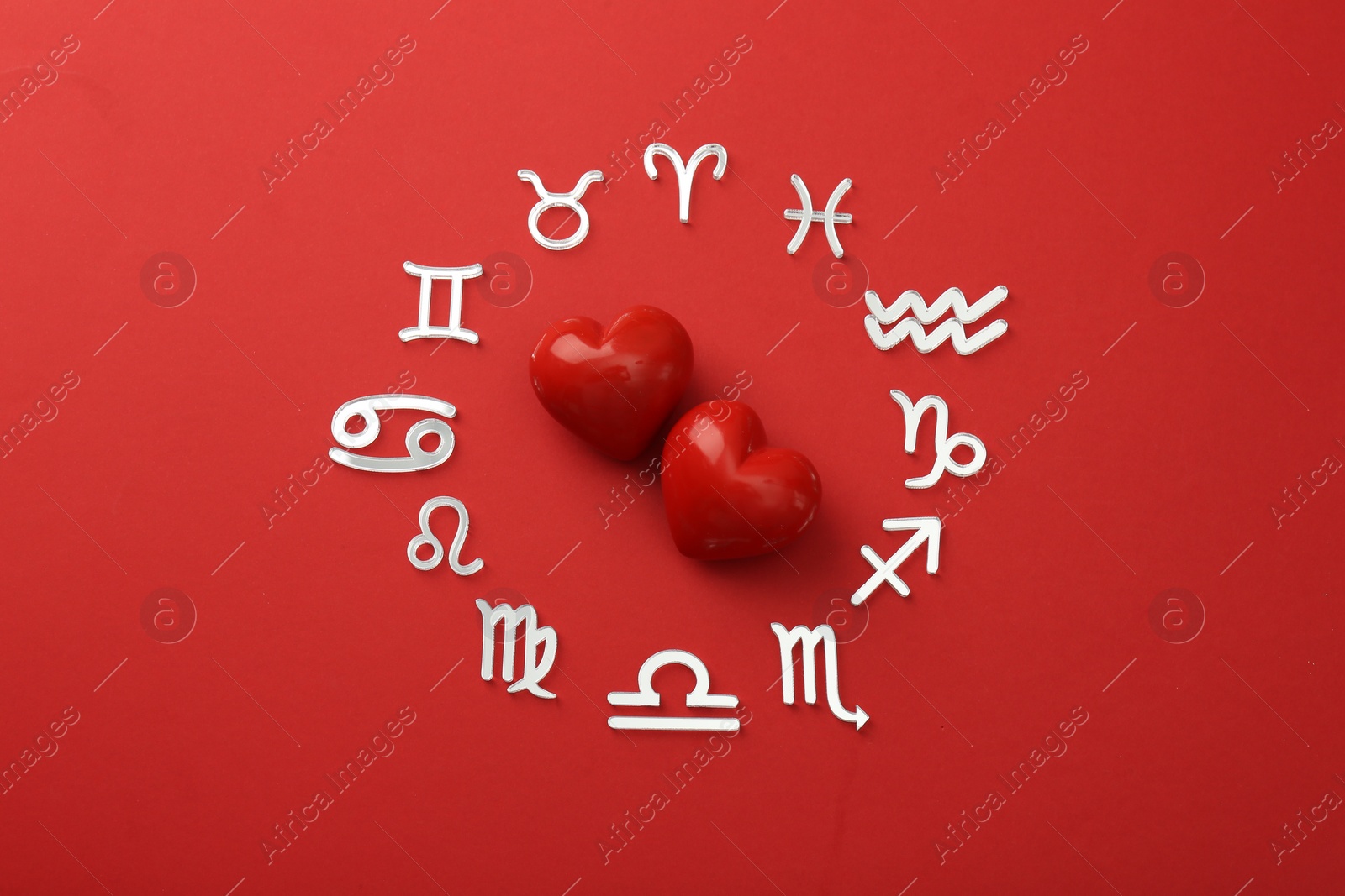 Photo of Zodiac signs and hearts on red background, flat lay