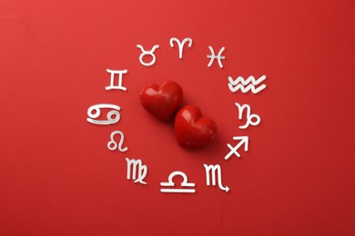 Photo of Zodiac signs and hearts on red background, flat lay