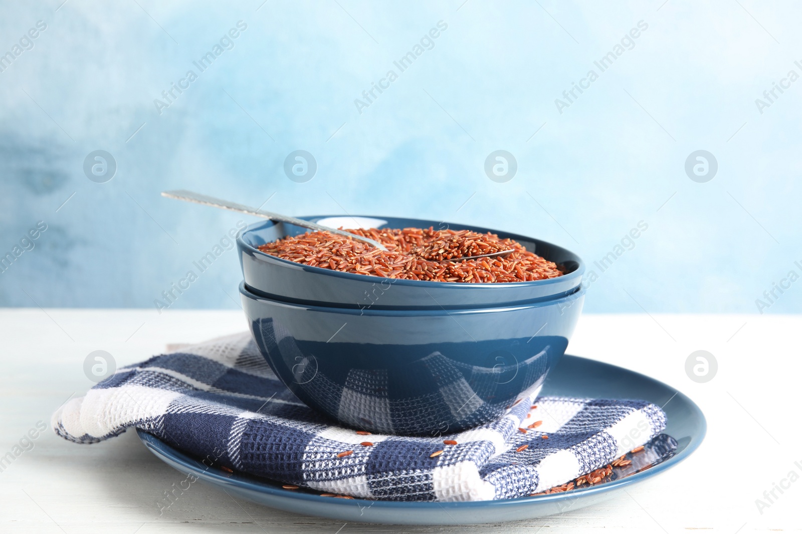 Photo of Bowl with uncooked red rice and spoon on white table