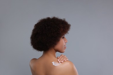 Photo of Beautiful young woman applying body cream onto back on grey background