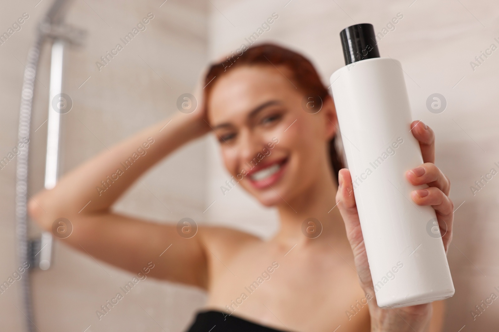Photo of Happy young woman with bottle of shampoo in shower, selective focus. Space for text