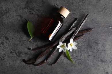 Photo of Vanilla pods, flowers, leaves and bottle with essential oil on grey textured table, flat lay