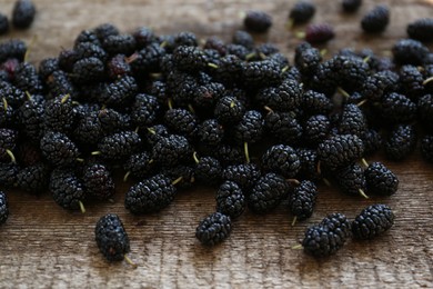 Photo of Heap of delicious ripe black mulberries on wooden table
