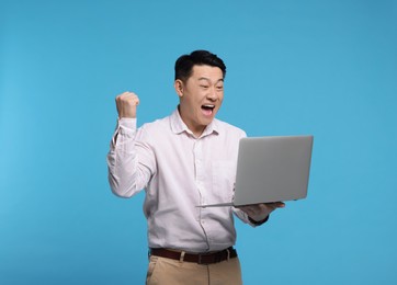 Emotional man with laptop on light blue background
