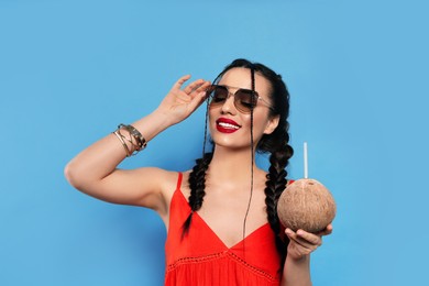 Young woman with fresh coconut on light blue background. Exotic fruit