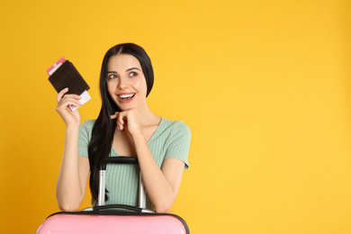 Photo of Beautiful woman with suitcase and ticket in passport for summer trip on yellow background. Vacation travel