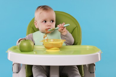 Photo of Cute little baby eating healthy food in high chair on light blue background