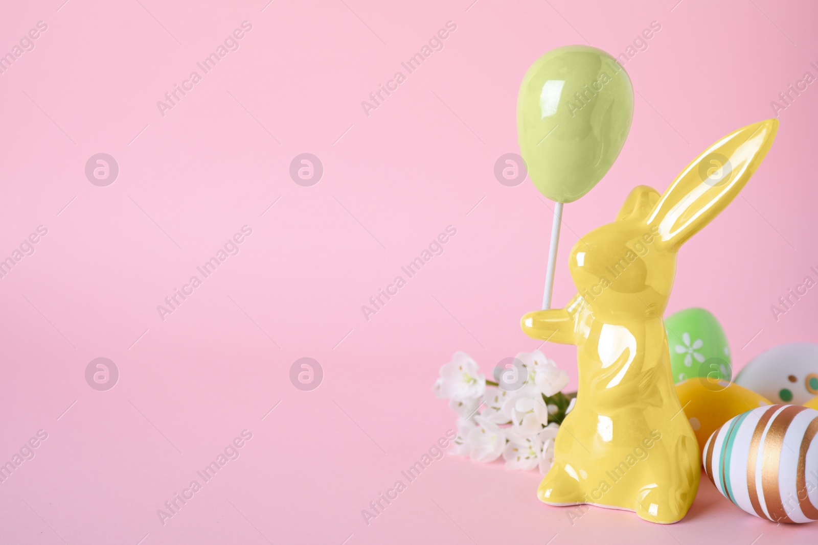 Photo of Easter bunny figure, flowers and decorated eggs on pink background. Space for text