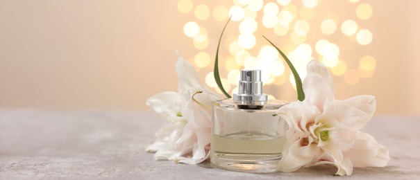 Photo of Bottle of perfume and beautiful lily flowers on table against beige background with blurred lights, space for text