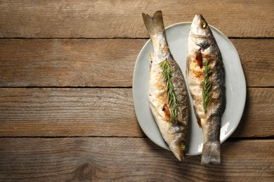 Photo of Delicious baked fish and rosemary on wooden table, top view. Space for text