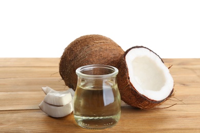 Photo of Ripe coconuts and jar with natural organic oil on wooden table against white background