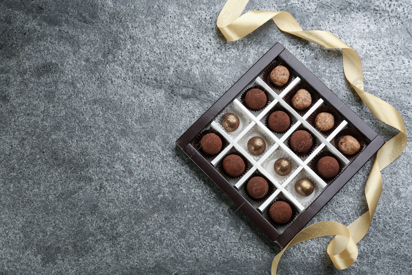 Photo of Different delicious chocolate candies in box and ribbon on grey table, top view. Space for text