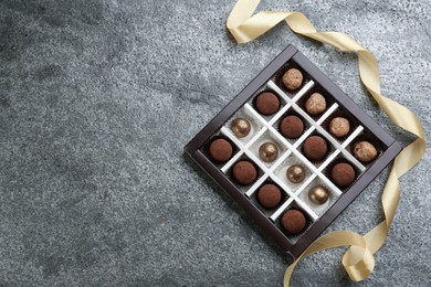 Different delicious chocolate candies in box and ribbon on grey table, top view. Space for text