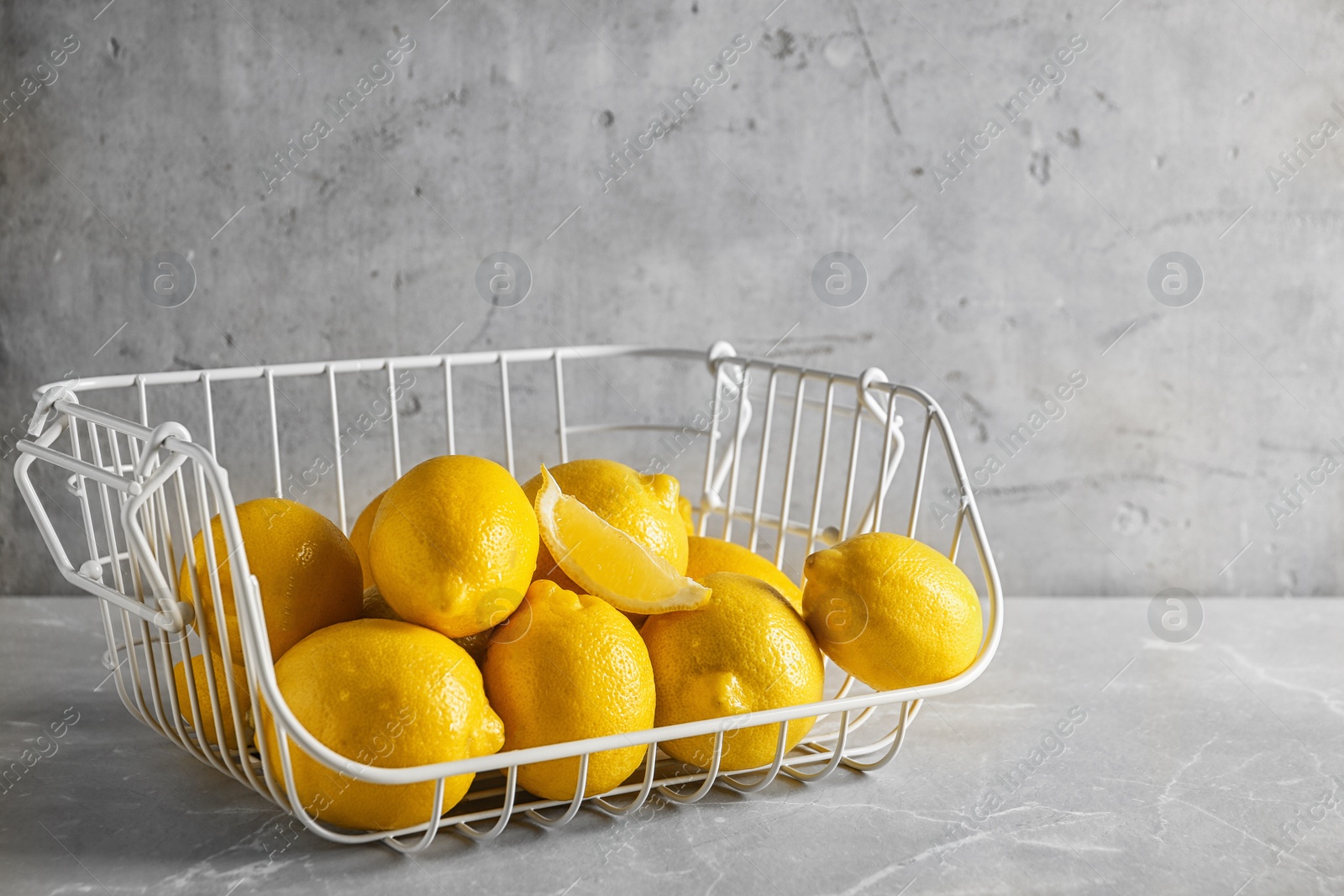 Photo of Metal basket with ripe lemons on table against light background