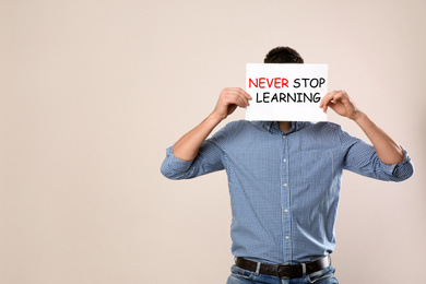 Image of Man holding paper with phrase NEVER STOP LEARNING on beige background. Space for text