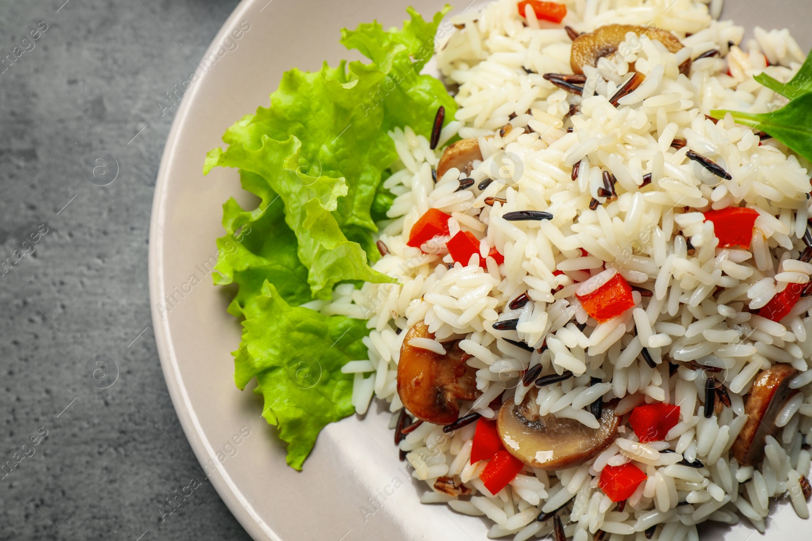 Photo of Delicious rice pilaf with mushrooms on grey table, closeup