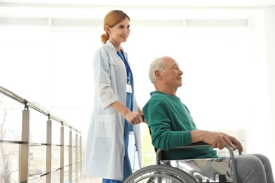 Photo of Nurse assisting elderly man in wheelchair indoors