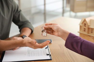 Photo of Real estate agent giving key with trinket to client in office, closeup