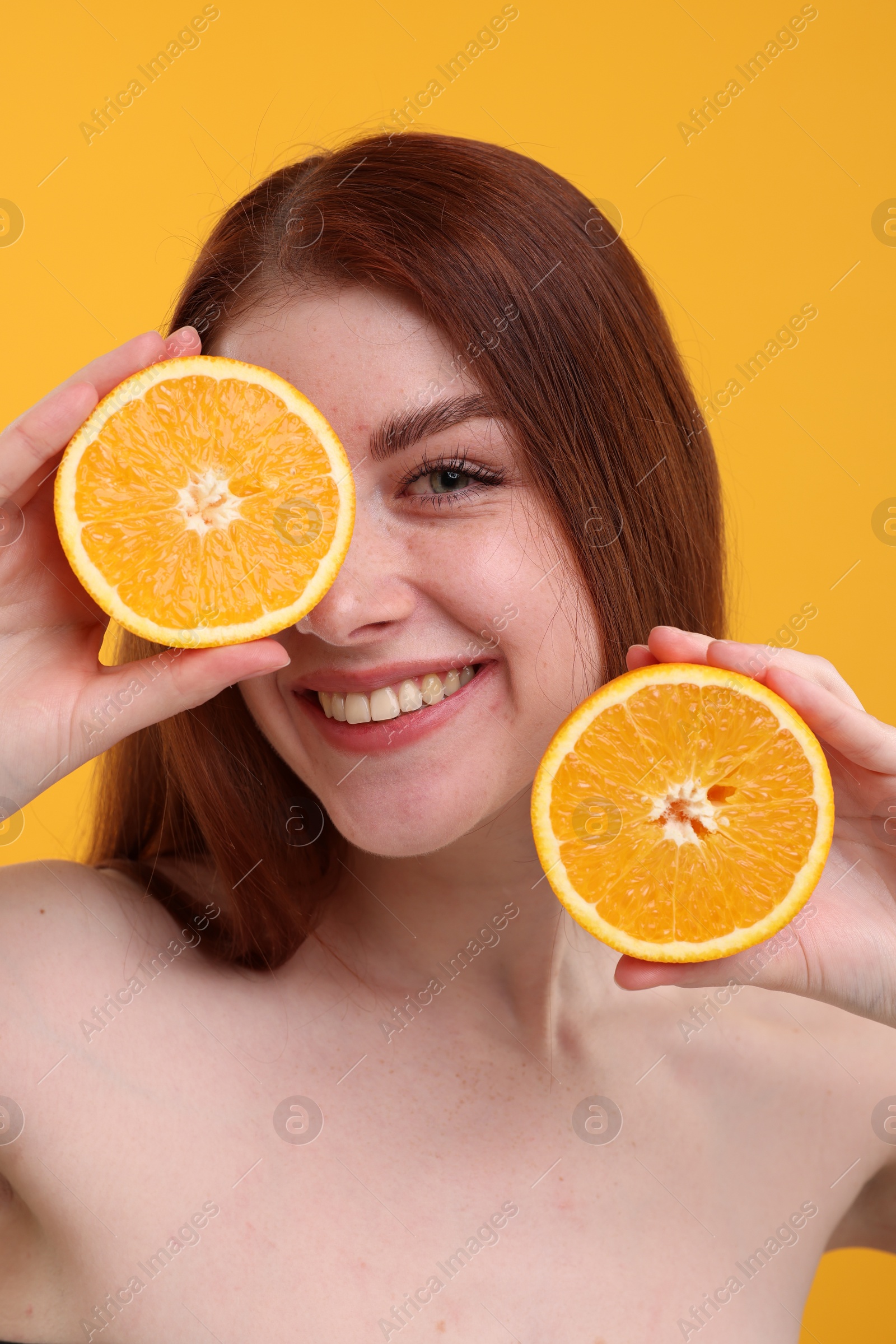 Photo of Smiling woman with freckles covering eye with half of orange on yellow background