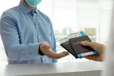 Agent giving passports and tickets to man with protective mask at check-in desk in airport, closeup