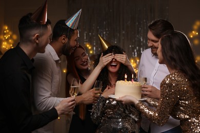 Happy friends with tasty cake and glasses of sparkling wine celebrating birthday indoors