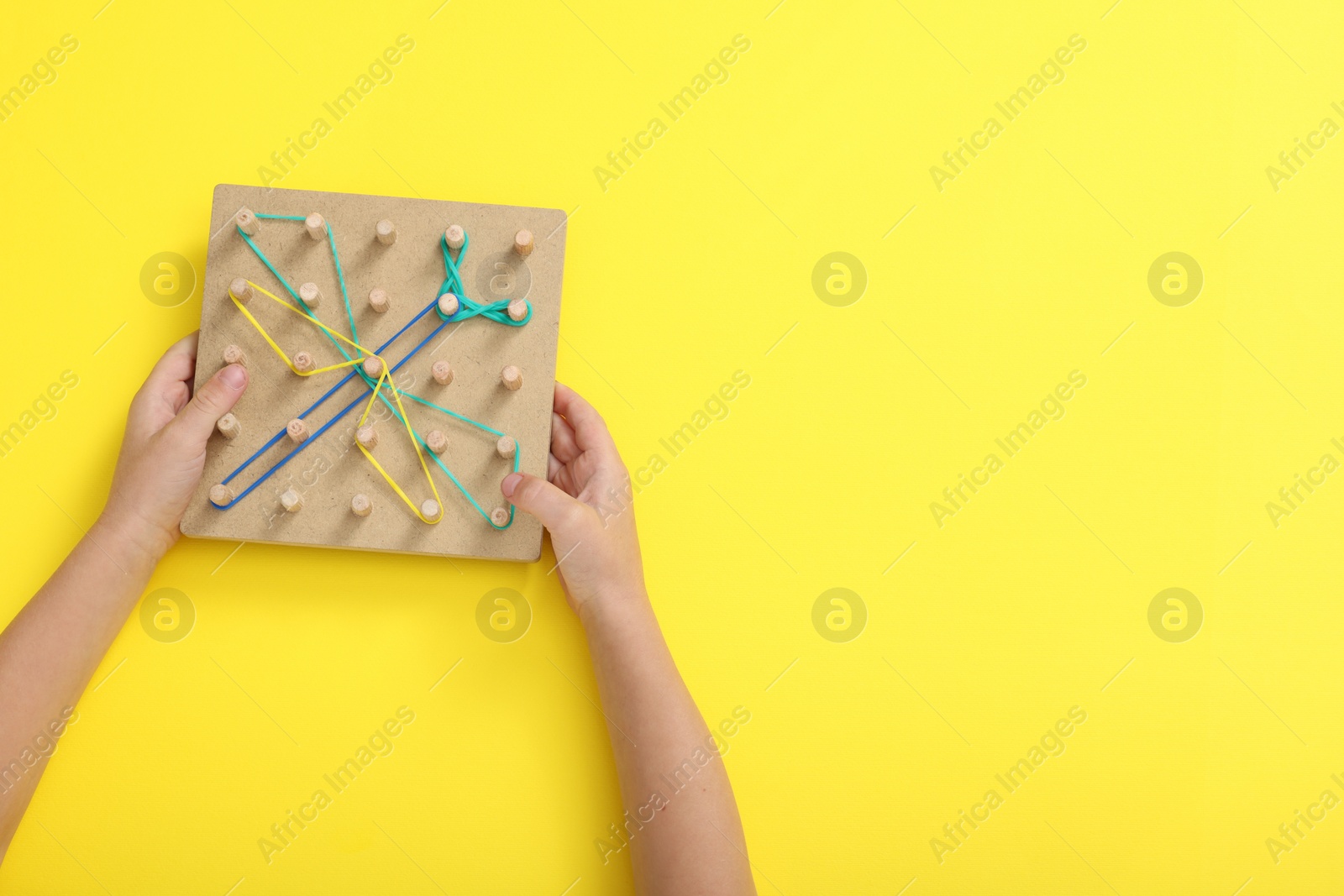 Photo of Motor skills development. Boy with geoboard and rubber bands at yellow table, top view. Space for text