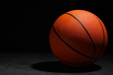 Basketball ball on grey stone table against dark background, space for text