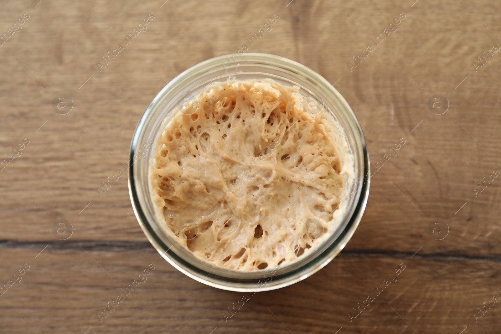 Photo of Sourdough starter in glass jar on wooden table, top view