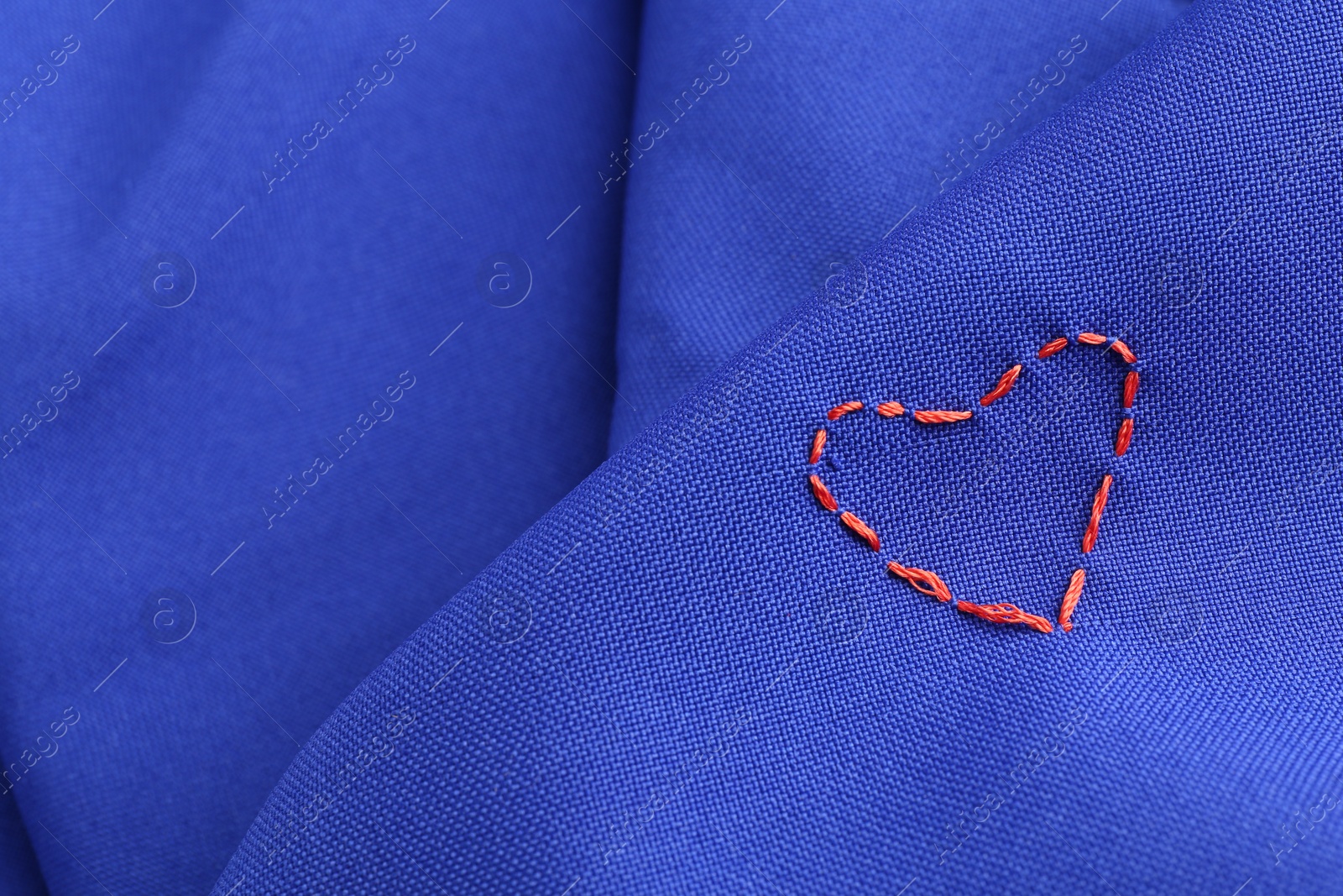 Photo of Red embroidered heart on blue cloth, closeup