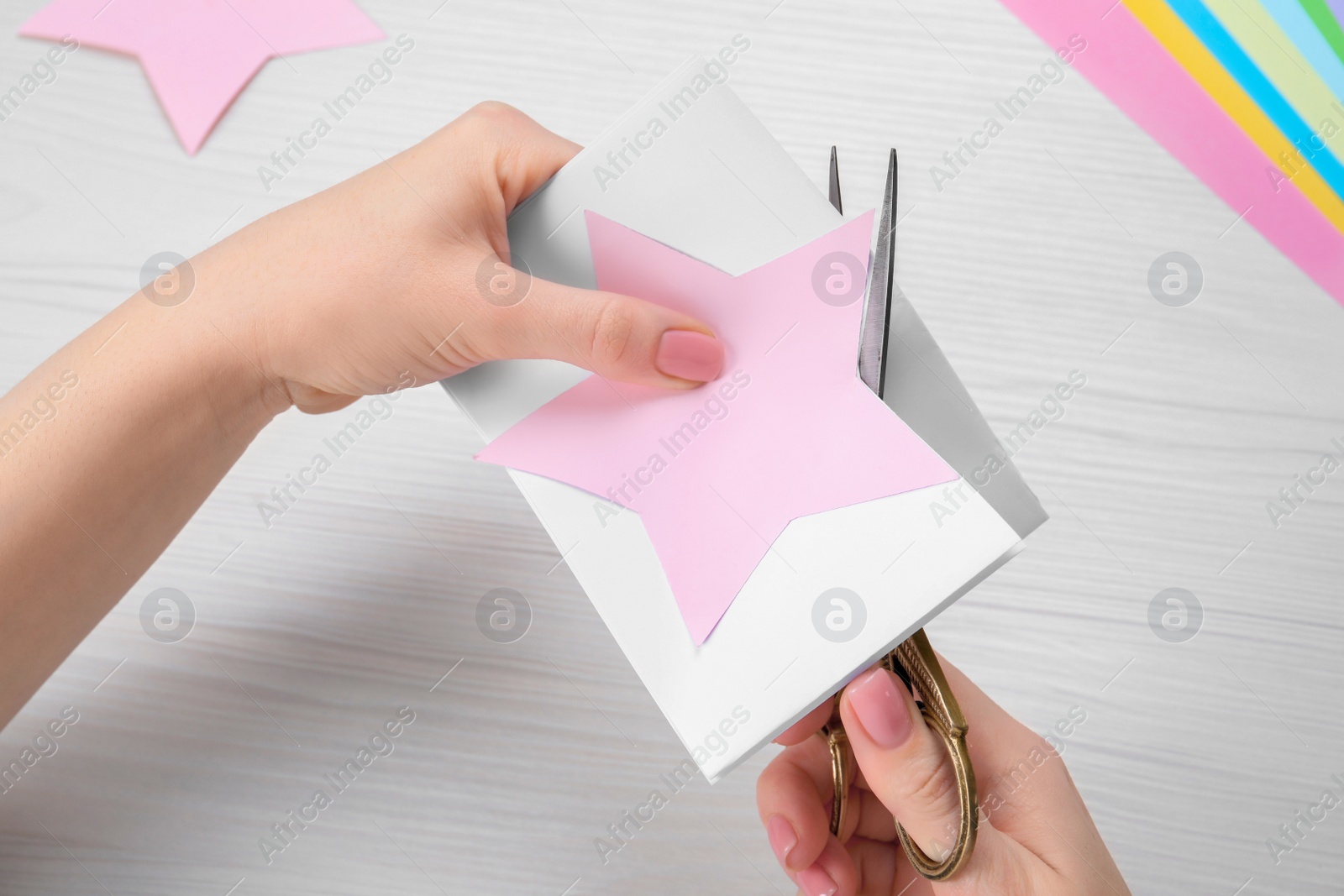 Photo of Woman cutting paper with scissors at white wooden table, top view