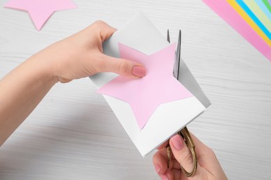 Woman cutting paper with scissors at white wooden table, top view